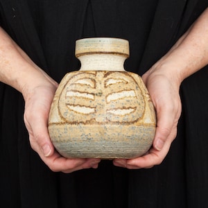 May include: A brown and white ceramic vase with a geometric design. The vase has a speckled glaze and a light blue rim.