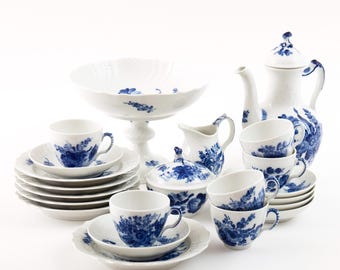 May include: A complete white porcelain tea set with blue floral designs. The set includes cups, saucers, plates, a sugar bowl, creamer, a serving bowl, and a teapot. The tea set is arranged on a white surface.