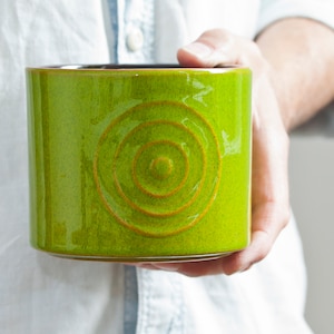 以下が含まれることがあります： 同心円模様の明るい緑色のセラミックプランター。プランターは茶色の縁取りがあり、光沢のある釉薬で覆われています。