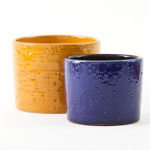 Puede incluir: Dos macetas de cerámica, una amarilla y otra azul. Ambas macetas tienen una superficie texturizada.