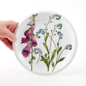 Puede incluir: Plato de cerámica blanco con un diseño floral con digitales rosas y nomeolvides azules.