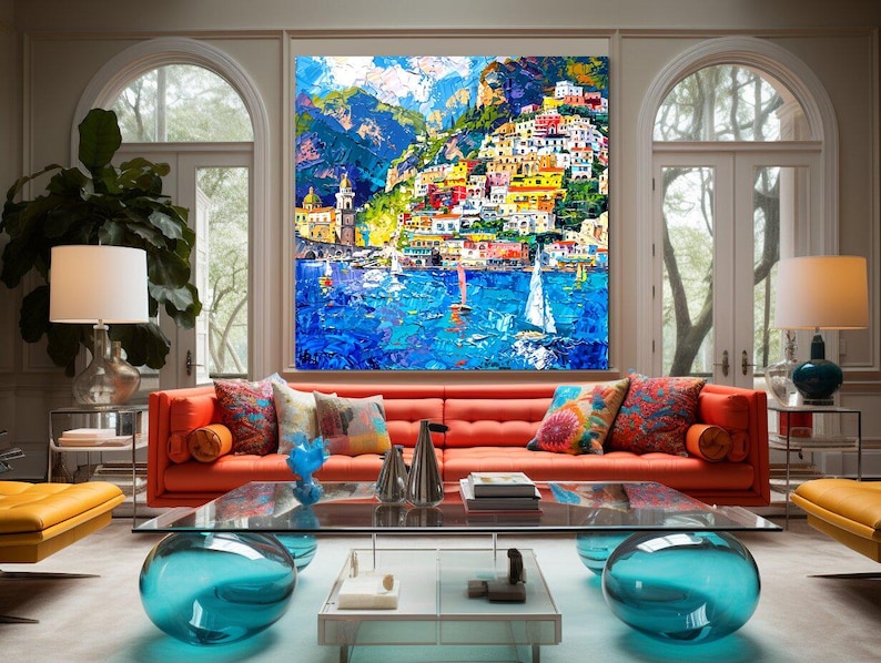 May include: A colorful painting of a seaside town with buildings on a hillside, boats in the water, and a blue sky with clouds. The painting is framed and hanging on a wall in a living room.