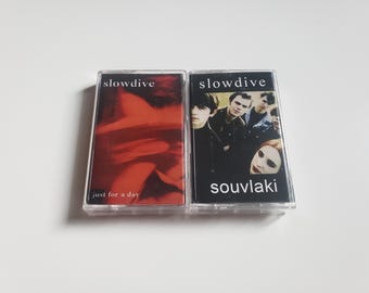 May include: Two cassette tapes by the band Slowdive. The first tape is titled "Just for a Day" and features a red and orange abstract design. The second tape is titled "Souvlaki" and features a black and white photo of the band members.