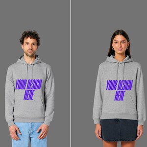 Peut inclure: Deux personnes portant des sweats à capuche gris avec le texte "YOUR DESIGN HERE" en violet. Les sweats à capuche ont une poche avant et une capuche à cordon. L'une porte un jean bleu, l'autre une jupe en jean.