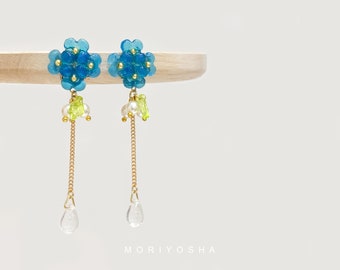 May include: A pair of blue flower dangle earrings with gold chains and clear teardrop crystals. The earrings feature small green beads and white pearls.