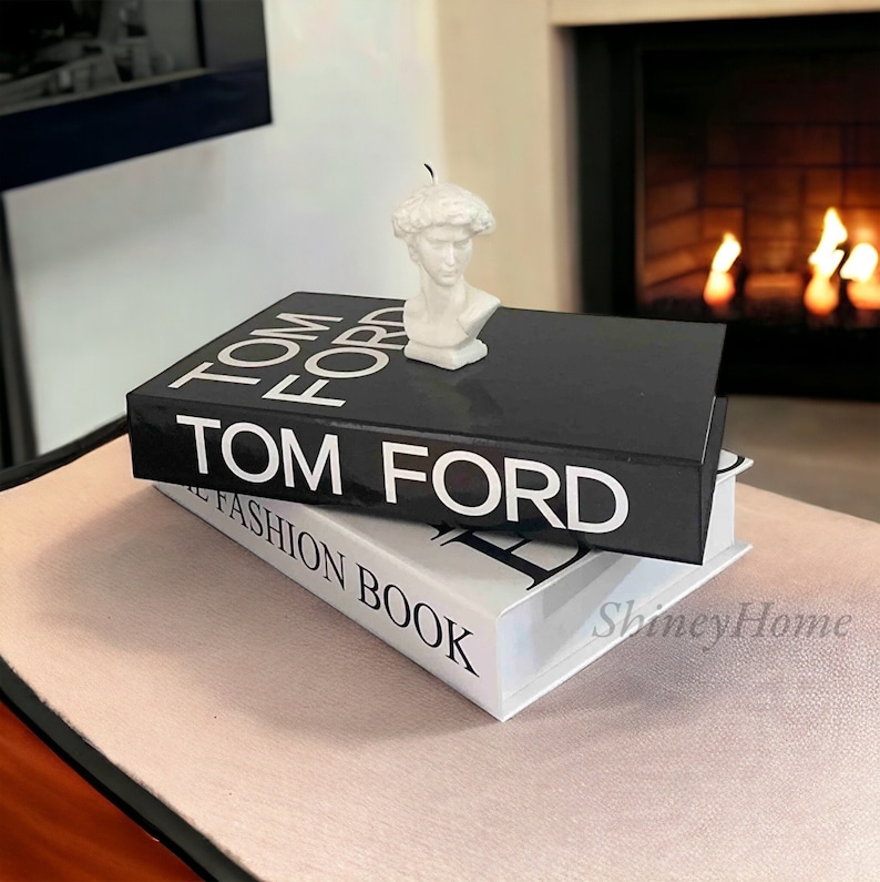 Peut inclure: Deux livres empil&eacute;s l'un sur l'autre. Le livre du dessus est noir avec du texte blanc qui dit "TOM FORD". Le livre du dessous est blanc avec du texte noir qui dit "THE FASHION BOOK". Un buste en pl&acirc;tre blanc d'un homme est pos&eacute; sur le livre noir.