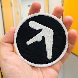 May include: A black and white embroidered patch with a white arrow pointing to the right. The patch is circular and has a white border.