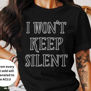 Może przedstawiać: Czarny t-shirt z białym napisem "I WON'T KEEP SILENT". Koszulka ma r&oacute;wnież białe koło z napisem "$5 from every shirt sold will be donated to the ACLU".