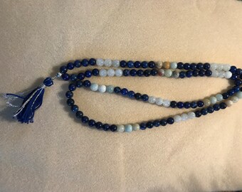 Könnte beinhalten: Eine blaue, weiße und braune Perlenkette mit einem Quastenanhänger. Die Kette besteht aus Lapislazuli-, Aquamarin- und Jaspisperlen.