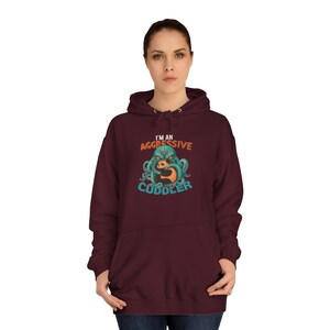 May include: A maroon hoodie with a graphic of a green octopus hugging a panda bear. The text "I'm an Aggressive Cuddler" is printed on the hoodie.