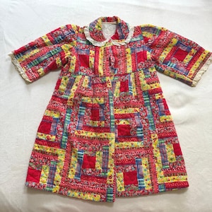May include: A quilted coat in a patchwork design, featuring red, yellow, and blue fabrics. The coat has a white lace collar and cuffs. The overall pattern is a mix of floral and geometric shapes, creating a vintage aesthetic.