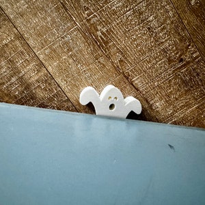 May include: A white ghost cutout with a surprised expression, peeking over the edge of a blue surface.