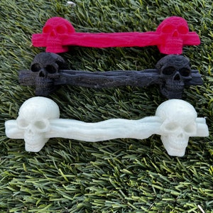 May include: Three skull-shaped drawer pulls in different colors. The top pull is red, the middle pull is black, and the bottom pull is white.