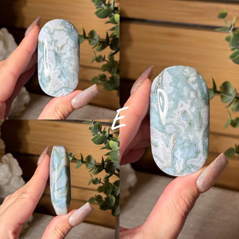 May include: A polished, oval-shaped stone with a marbled pattern of pale green, white, and gray. The stone is held in a hand, showcasing its smooth, rounded form. The natural stone has a unique, organic appearance.