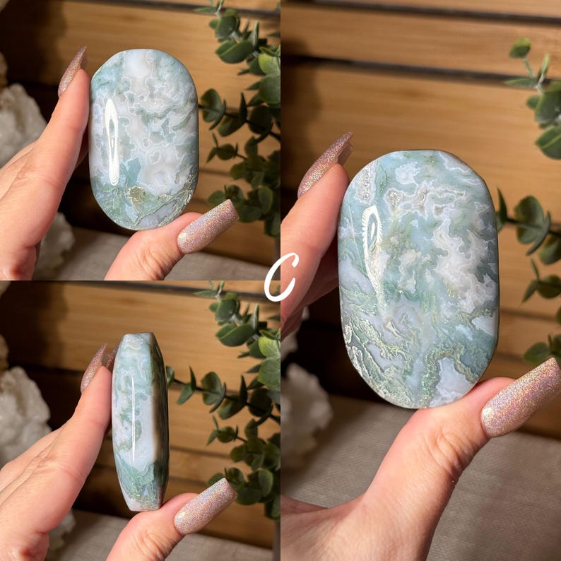 May include: A polished, oval-shaped gemstone with a swirling pattern of white and light green. The stone is held in a hand, showcasing its smooth surface and natural variations. The gemstone is a decorative item.