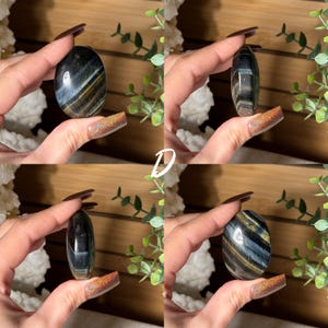 May include: Four images of an oval-shaped polished stone with blue, black, and gold bands. The stone is held in a hand against a wooden background with greenery. The letter "D" is in white in the center of the image.