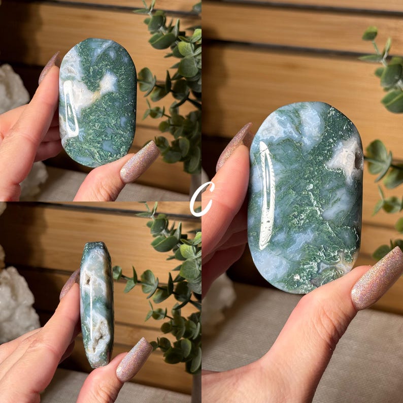 May include: A polished, oval-shaped moss agate stone. The stone features a mix of green, white, and translucent areas, creating a natural, organic pattern. The stone is held in a hand, showcasing its smooth surface and unique coloration.