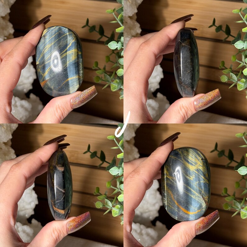 May include: Four polished gemstones with a mix of blue, gold, and black colors. The stones are oval-shaped and held in a hand. The background includes greenery and a wooden surface.