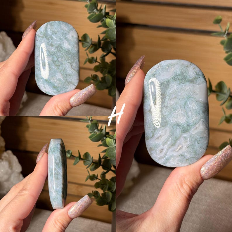 May include: A polished, oval-shaped stone with a swirling pattern of pale green and white. The stone has a smooth, rounded top and a flat bottom. The stone is held in a hand, showcasing its natural beauty and unique design.