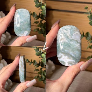 May include: A polished, oval-shaped gemstone with a swirling pattern of white and green. The stone is held in a hand, showcasing its smooth surface and natural color variations. The gemstone is a decorative item.