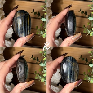 May include: Four images of a polished, oval-shaped gemstone. The stone has a dark base color with streaks of blue and gold. The gemstone is held in a hand, with a background of greenery and a wooden surface.