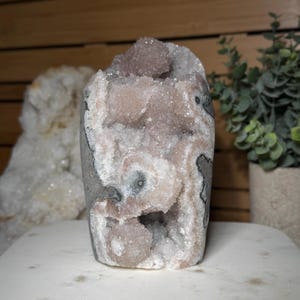 May include: A large, natural amethyst geode with a light purple hue. The geode features a crystalline structure with a mix of white, gray, and purple colors. The geode is displayed on a white surface.