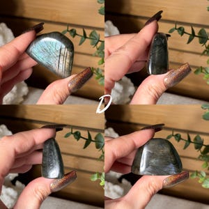May include: Four polished labradorite stones are displayed, each with unique shapes and iridescent flashes of blue, green, and gold. The stones are held up against a natural background, showcasing their natural beauty. The letter "D" is visible in white.