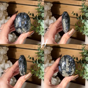 May include: Four views of a polished oval stone with a speckled pattern of black, gray, and blue. The stone is held in a hand, showcasing its smooth, rounded shape and natural color variations. The stone is a decorative item.