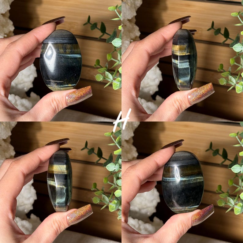 May include: An oval-shaped, polished gemstone with bands of dark blue, gold, and teal. The stone is held in a hand, showcasing its smooth, reflective surface. The gemstone is a natural, decorative item.