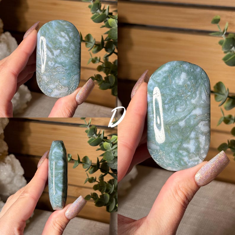 May include: A polished, oval-shaped stone with a marbled pattern of green and white. The stone is held in a hand, showcasing its smooth surface and natural variations. The stone's shape is rounded at the ends and has a flat back.