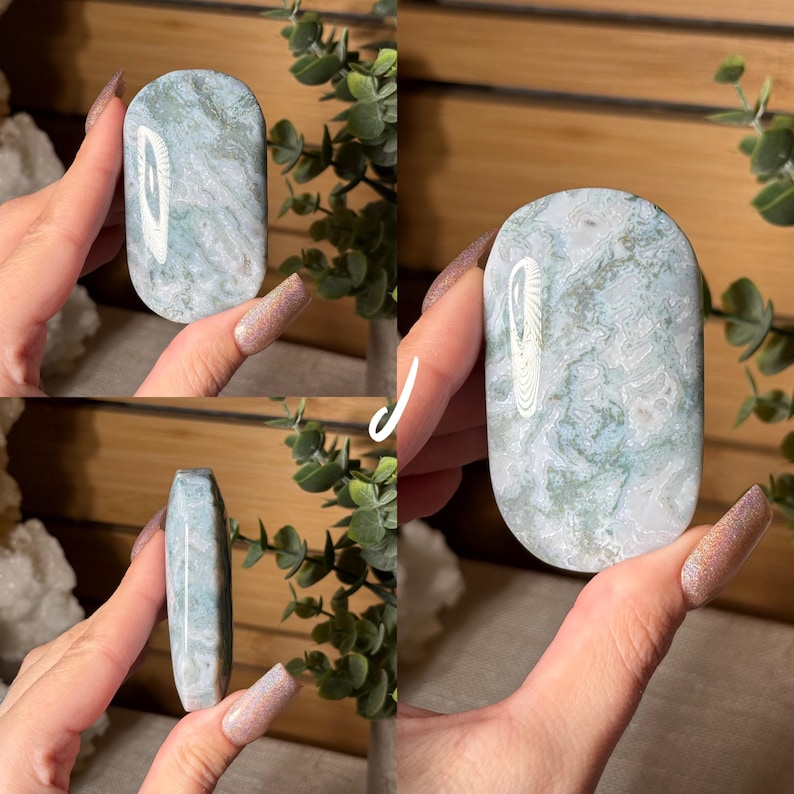 May include: A polished, oval-shaped stone with a marbled pattern of white and pale blue-green. The stone is held in a hand, showcasing its smooth, rounded edges and natural variations. The stone's surface reflects light, highlighting its unique texture and color.