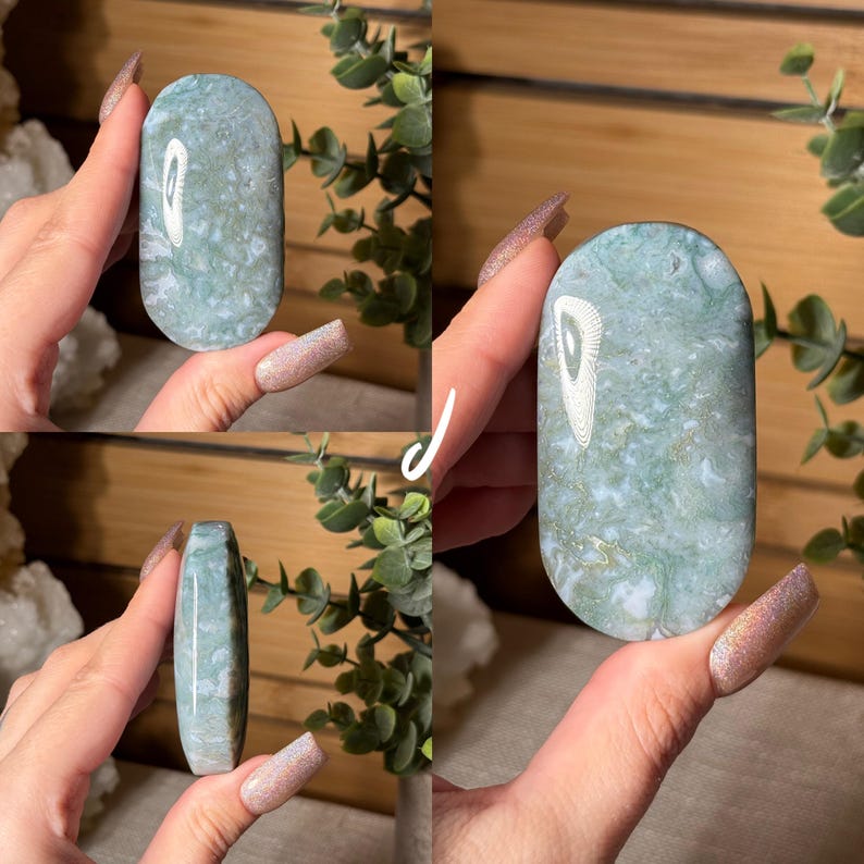 May include: A polished, oval-shaped gemstone with a mottled pattern of pale green, white, and gold. The stone is held in a hand, showcasing its smooth surface and natural variations. The gemstone is a decorative item.