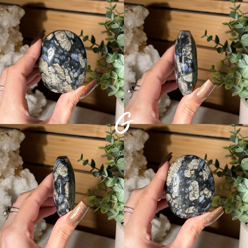 May include: A polished, oval-shaped stone with a dark blue and gray mottled pattern, accented with lighter beige and blue inclusions. The stone is held in a hand, showcasing its smooth, rounded form. The stone's surface reflects light, highlighting its unique mineral composition.