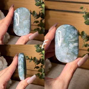 May include: A collection of polished, oval-shaped gemstones in shades of blue and green, with intricate patterns. The stones are held up against a backdrop of greenery, showcasing their natural beauty and unique textures. The letter "F" is visible in white.