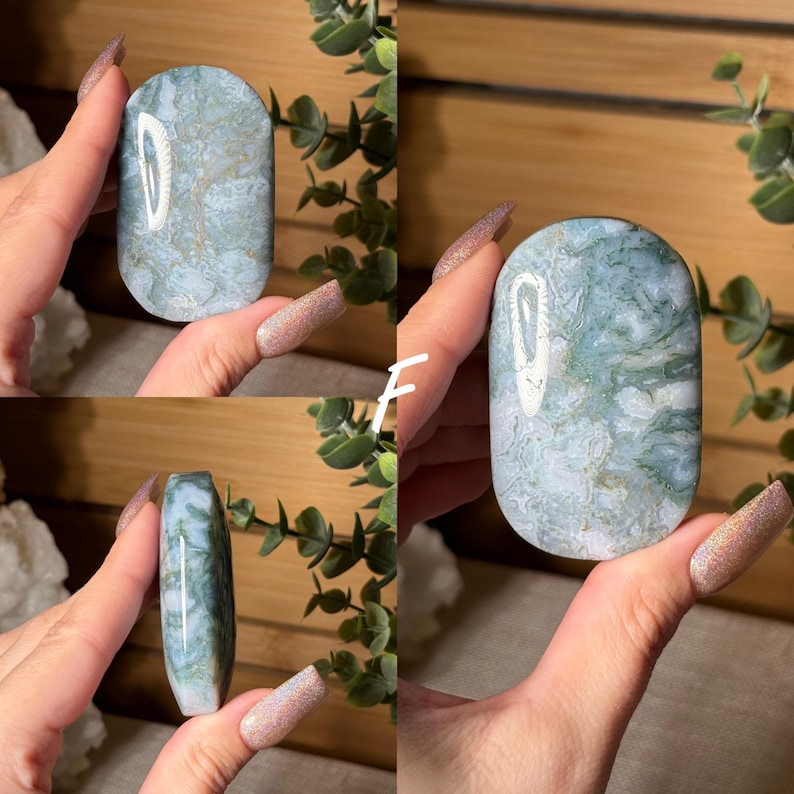 May include: A collection of polished, oval-shaped gemstones in shades of blue and green, with intricate patterns. The stones are held up against a backdrop of greenery, showcasing their natural beauty and unique textures. The letter "F" is visible in white.