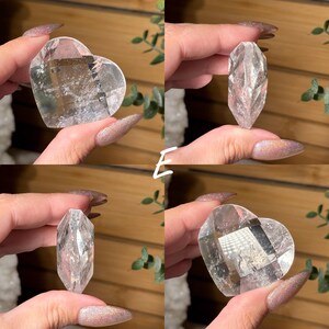 Puede incluir: Cuatro piezas de cristal de cuarzo transparente. Dos tienen forma de coraz&oacute;n y dos son cristales alargados y facetados. Los cristales se sostienen contra un fondo borroso de vegetaci&oacute;n y madera. Los cristales son transparentes y reflejan la luz.