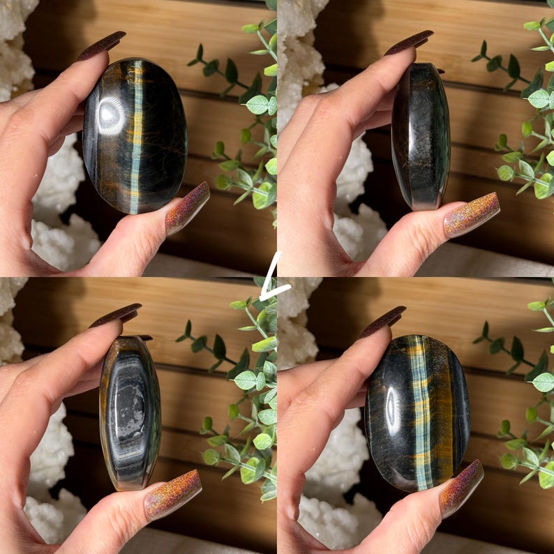 May include: A polished, oval-shaped tiger's eye stone. The stone features bands of dark brown, gold, and blue-green hues. The stone is held in a hand, showcasing its smooth, reflective surface.