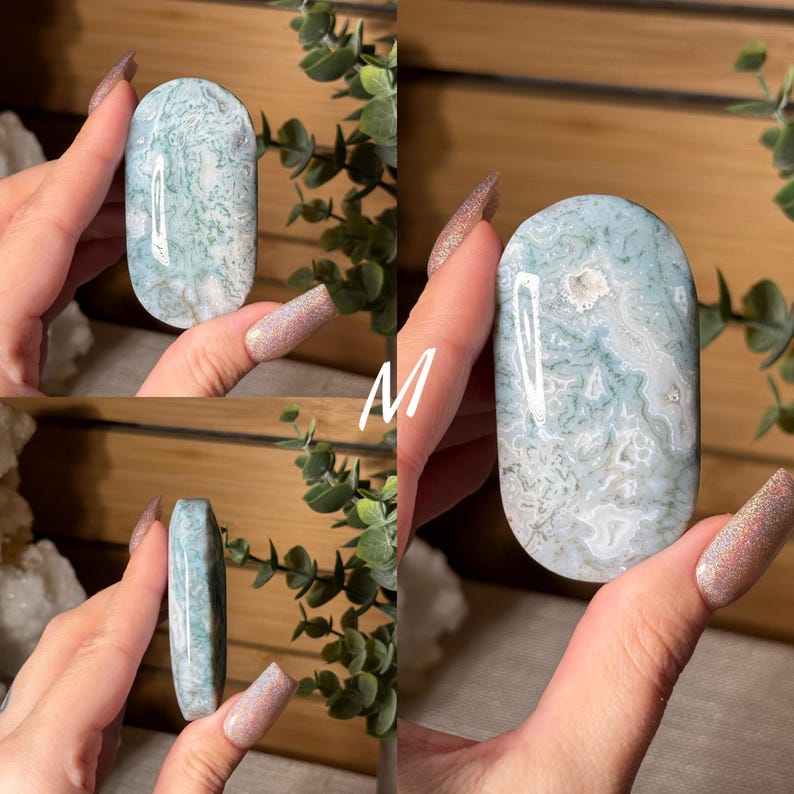 May include: A polished, oval-shaped gemstone with a light blue and white pattern. The stone has a smooth surface and is held in a hand. The gemstone is a natural mineral, likely used for decorative or metaphysical purposes.