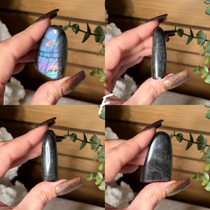 May include: Four images of polished gemstones. One is a blue, purple, and gold labradorite. The other three are dark gray stones with a smooth, polished finish. The stones are held in a hand with long, dark nails.