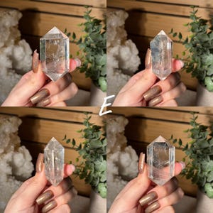 May include: Four clear quartz crystal points are displayed, each held by a hand. The crystals have a faceted, pointed shape. The background includes greenery and a wooden surface, with a white crystal cluster visible.