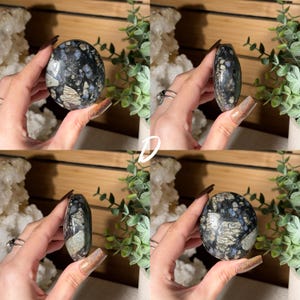 May include: Four views of a polished, oval-shaped gemstone. The stone features a mix of dark blue, gray, and white patterns. The gemstone is held in a hand, showcasing its shape and texture. The background includes greenery and a wooden surface.