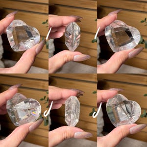 Puede incluir: Coraz&oacute;n de cristal de cuarzo transparente y punta de cristal. El cristal en forma de coraz&oacute;n est&aacute; facetado y es transparente, con inclusiones internas visibles. La punta de cristal tambi&eacute;n es clara y facetada. Sobre fondo de madera.