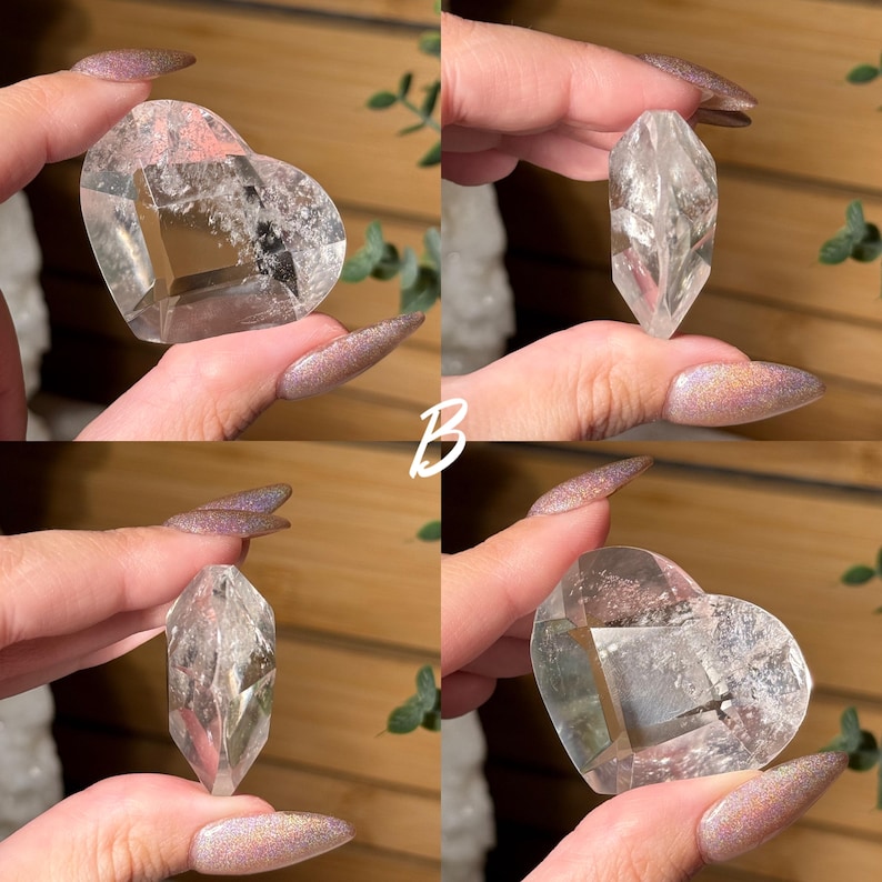 Puede incluir: Se muestran cuatro cristales de cuarzo transparente. Dos tienen forma de coraz&oacute;n y dos son puntiagudos. Los cristales son transparentes con inclusiones internas. El fondo es una superficie de madera con follaje verde. La letra "B" es visible.