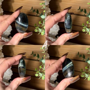 May include: Four polished, oval-shaped gemstones are displayed. Each stone features a mix of dark blue, gray, and gold colors, with light blue bands. The gemstones are held in a hand, showcasing their smooth, polished surfaces. The letter "A" is visible.