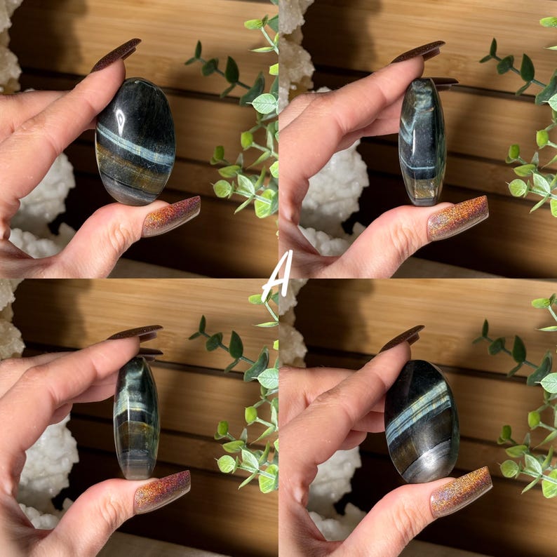 May include: Four polished, oval-shaped gemstones are displayed. Each stone features a mix of dark blue, gray, and gold colors, with light blue bands. The gemstones are held in a hand, showcasing their smooth, polished surfaces. The letter "A" is visible.