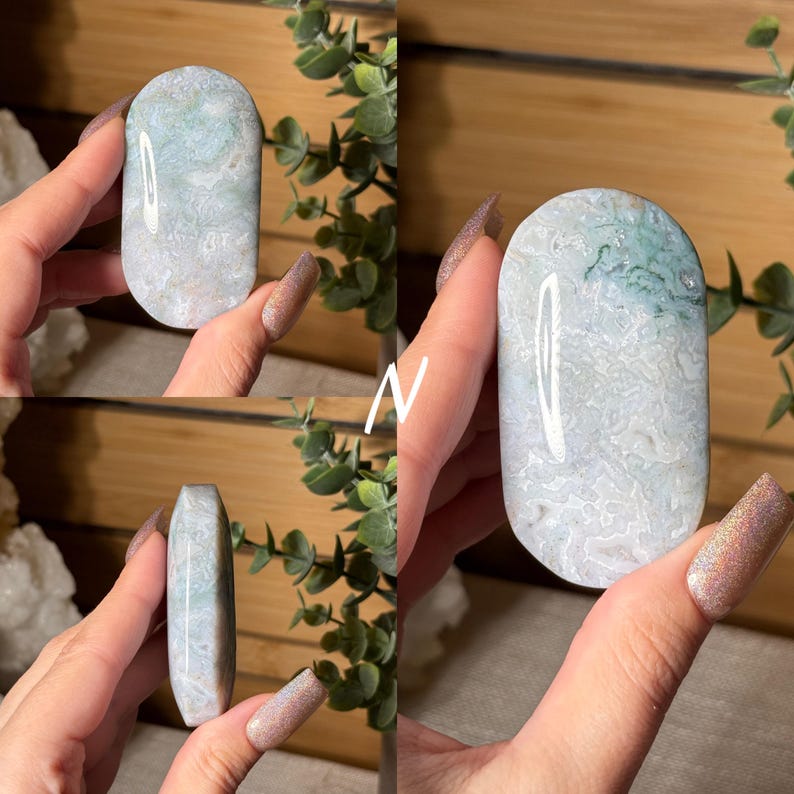 May include: A polished, oval-shaped stone with a marbled pattern of white, light blue, and green hues. The stone is held in a hand, showcasing its smooth surface and natural variations. The stone's shape is elongated, with rounded edges.