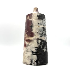 Peut inclure: Un grand vase cylindrique en céramique avec un col effilé, présentant une finition de surface marbrée dans des tons de bordeaux profond, noir charbon et blanc cassé. La texture semble patinée et organique, avec des dégradés de couleurs.