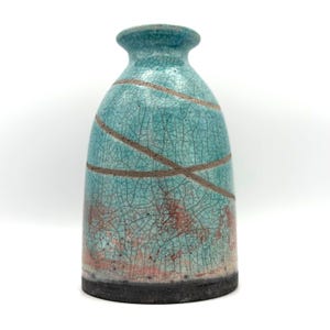 May include: A ceramic vase with a flared rim and a tapered body featuring a turquoise crackle glaze finish. The surface is decorated with two diagonal brown lines and a reddish-brown gradient near the base, which is finished in solid black.