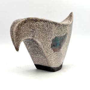 May include: A ceramic bird figurine featuring a cream-coloured glaze with a dark, intricate crackle pattern throughout. The base is a solid dark brown, and a single wing area displays a patch of iridescent blue and copper-toned glaze accents.