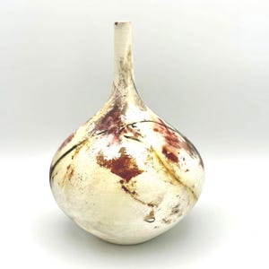 May include: A handmade ceramic vase with a rounded body and a thin neck. The vase has a cream-coloured base with reddish-brown and black abstract markings. The vase is a decorative item for the home.